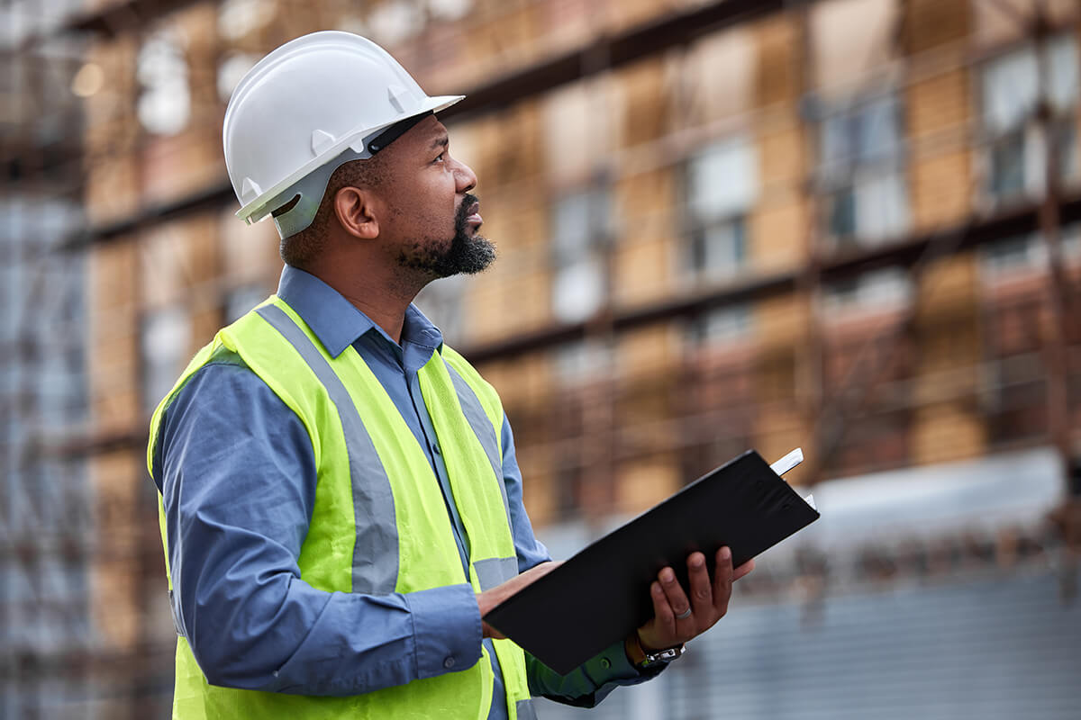 homme-casque-professionnel-devant-immeuble-tient-dossier